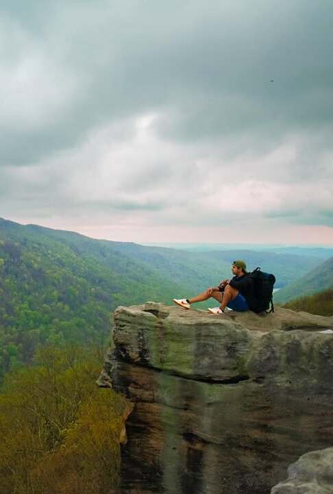 Sumesh Ramasamy sitting on a rock ledge overlooking the West Virginia mountains